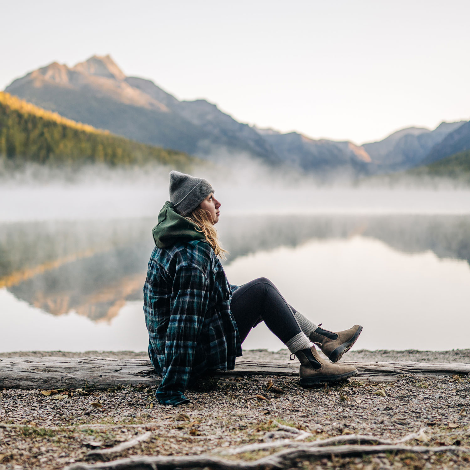 Jessica sitting on a log at sunrise at Bowman Lake in Glacier National Park.