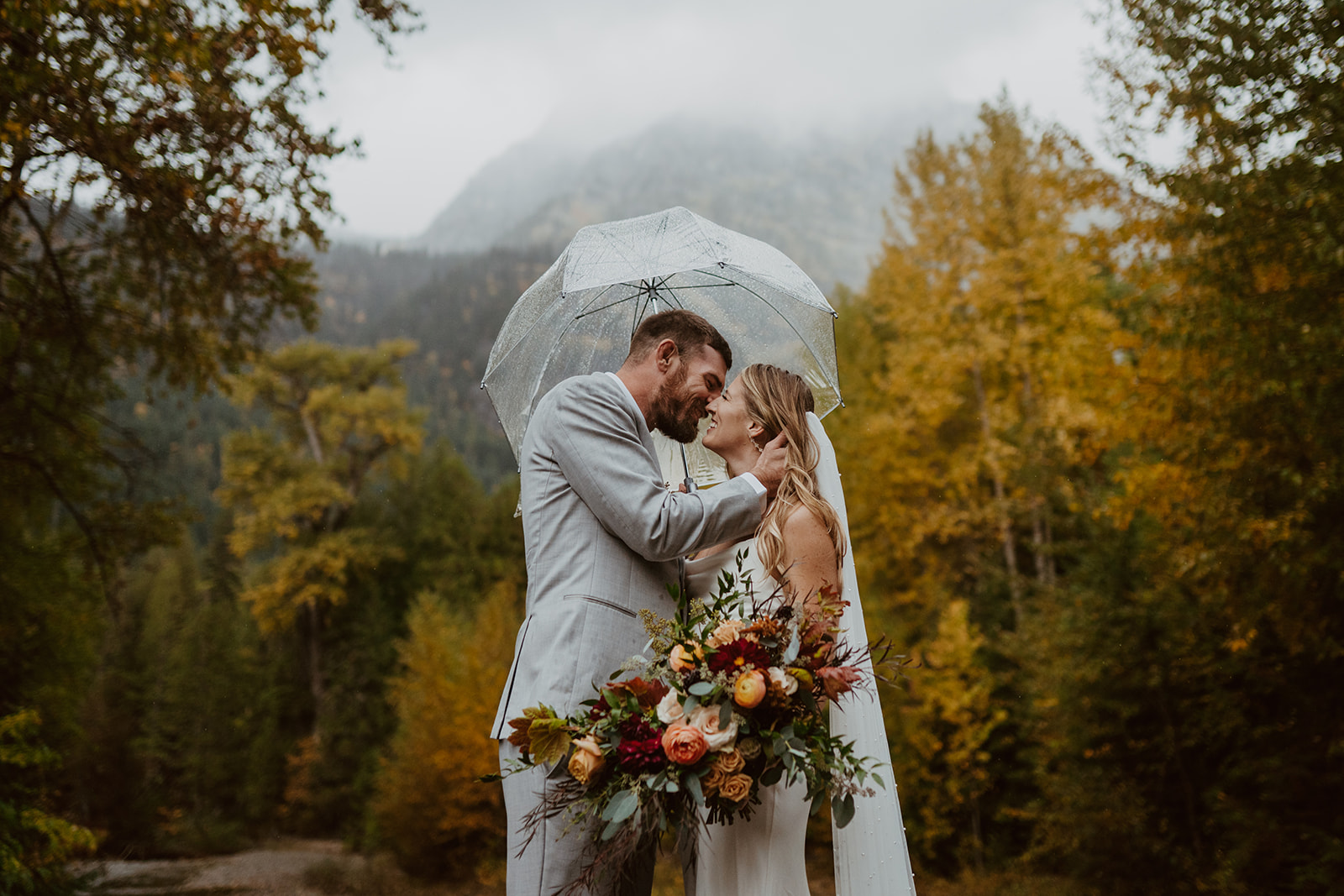 Weston and Kelsey during their fall elopement in Montana surrounded by oranged-leaves on trees and a mountain in the background.