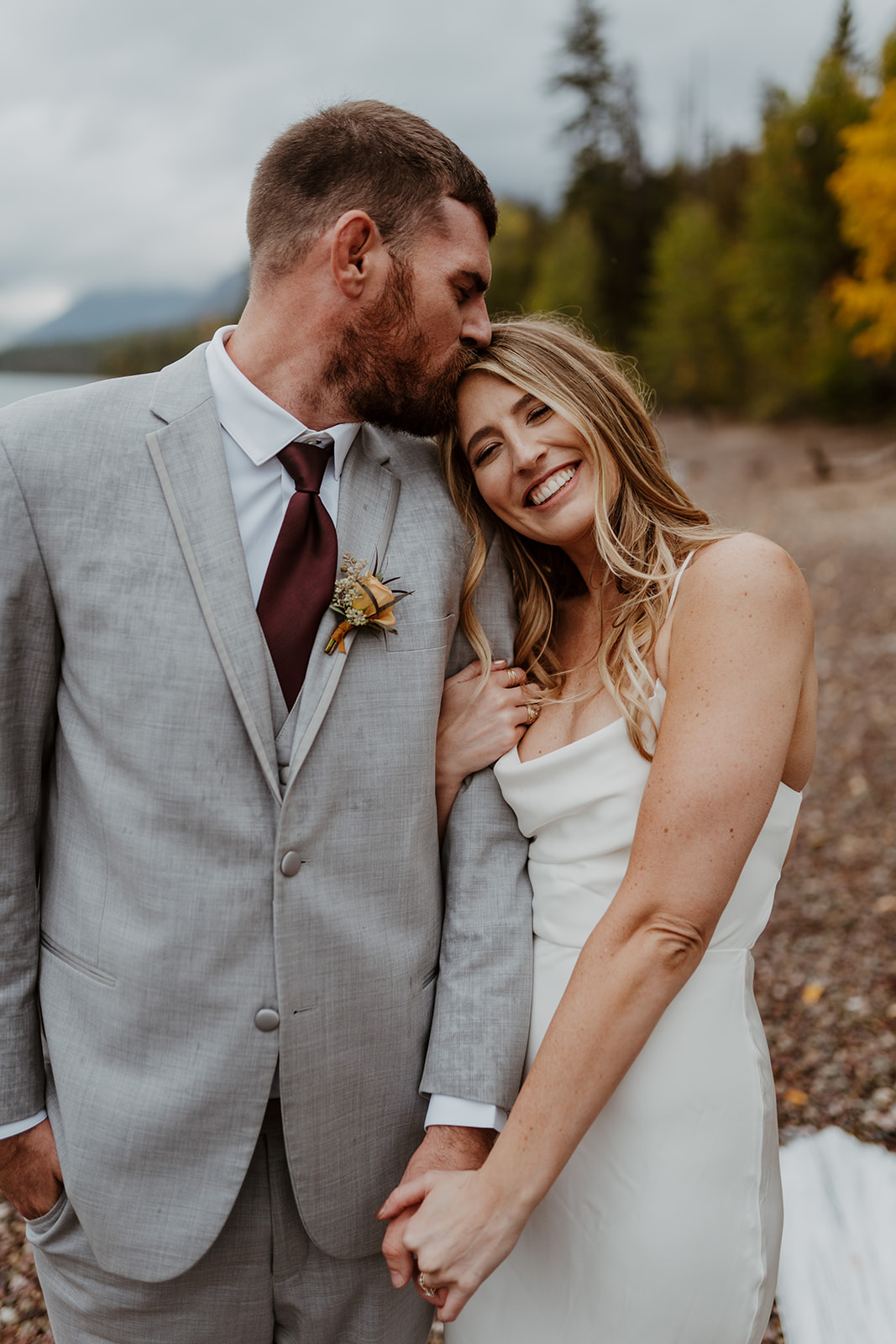 Kelsey smiling as Weston kisses the top of her head during their wedding in Glacier National Park.