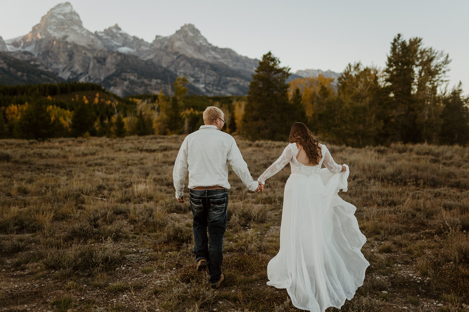 A couple running hand-in-hand through an open field after having their wedding in Grand Teton National Park.